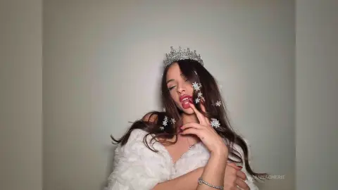 Glamorous woman in a white faux fur coat and silver crown posing with a dreamy, elegant expression.