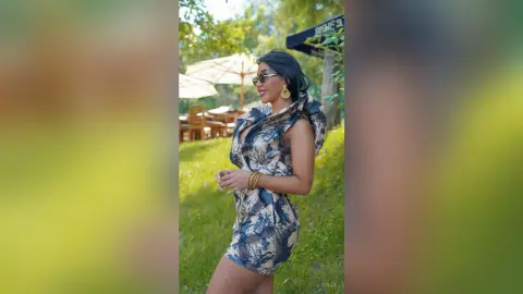 Dolce smiles in a blue and white floral print romper while standing on a grassy lawn outdoors.