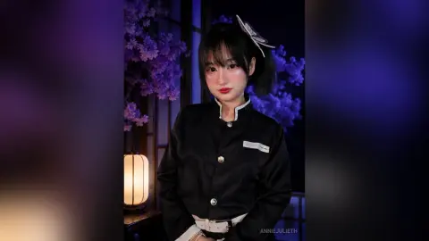 Young woman in black school uniform posing against purple floral background with a soft, moody aesthetic.
