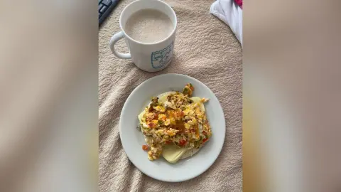 A steaming cup of coffee next to a plate of savory breakfast scramble on a cozy textured tablecloth.