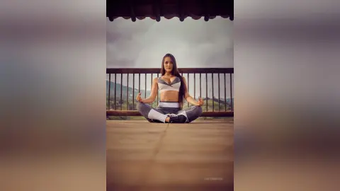 Serene woman in grey yoga outfit practicing meditation on a wooden balcony overlooking misty mountains.