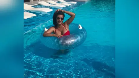 MissyJolie wears a red bikini while floating in a blue inflatable ring in a swimming pool.