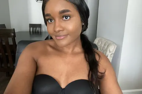 Smiling Black woman in a black strapless top posing in a bright indoor dining room setting.