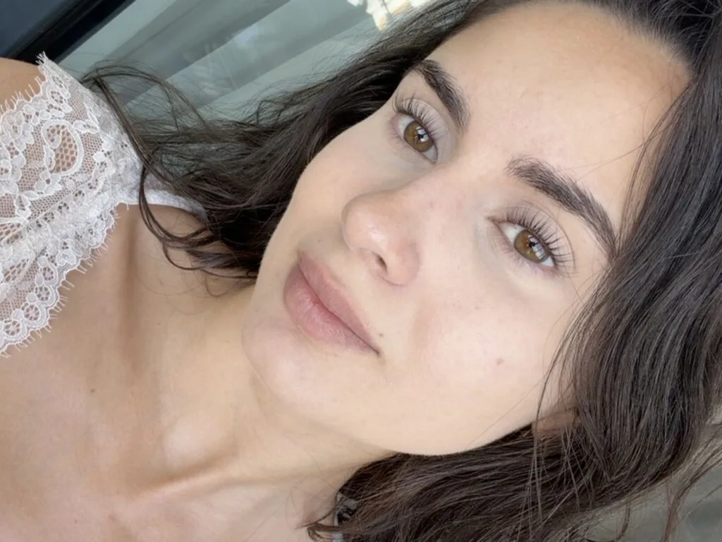 Grace looks into the camera with long dark hair and a white lace top.