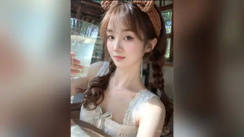Young woman in a white lace dress with a brown bow headband holding a refreshing drink in a sunny cafe.