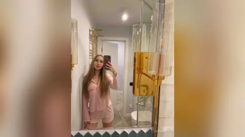 Young woman in pink loungewear taking a mirror selfie in a modern, bright bathroom.