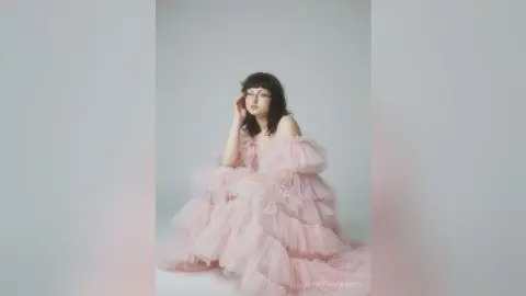 Elegant woman in a voluminous pink tulle gown posing in a minimalist studio setting with a dreamy mood.