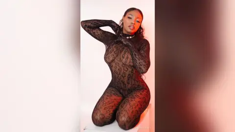 Elegant woman in a black sheer snakeskin bodysuit posing against a white studio background with moody red lighting.