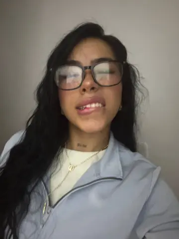 Young woman with long dark hair and glasses wearing a light blue zip-up jacket in a casual indoor setting.