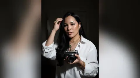Elegant woman in a white button-down shirt holding a vintage camera in moody, dramatic lighting.