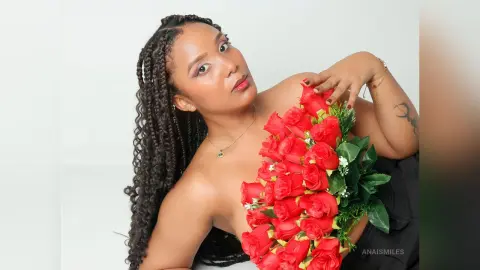 Beautiful woman with long braids holding a red rose bouquet in a bright, elegant studio setting.