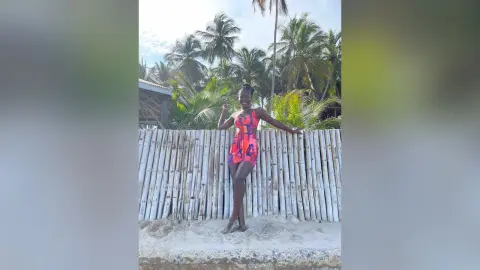Smiling woman in a colorful patterned swimsuit posing by a bamboo fence at a tropical beach resort.