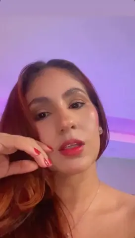 Portrait of a woman with reddish hair and red lipstick posing in soft purple lighting.