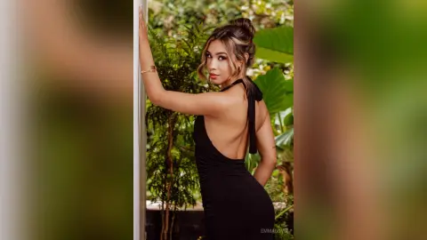 Elegant woman in a black backless evening dress posing in a lush tropical garden setting.