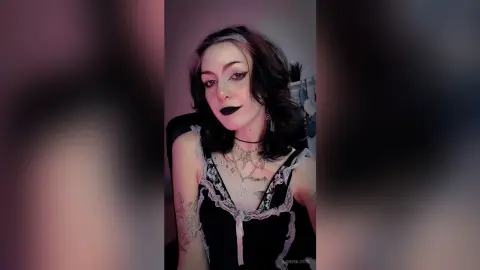 Gothic woman with dark makeup and black lace camisole posing in a moody indoor setting.