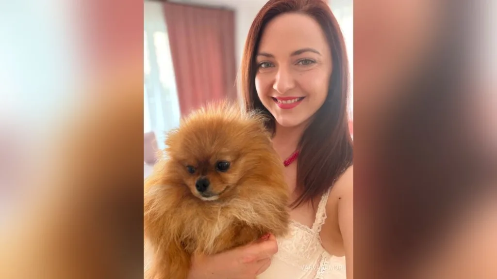 VarvaraMori — VarvaraMori smiles while holding a small brown Pomeranian dog in a white lace top.