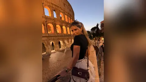 Stylish woman in a black top and white skirt posing in front of the historic Roman Colosseum at sunset.