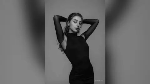 Elegant woman in a black long-sleeve bodysuit posing against a minimalist gray background in a moody portrait.