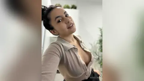 Smiling young woman in a beige ribbed cardigan posing in a bright, modern indoor setting.
