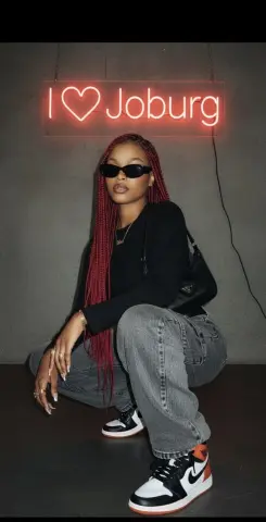 Stylish woman in black top and baggy jeans posing under a glowing I Love Joburg neon sign.