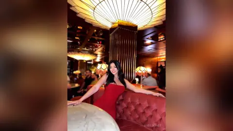 Elegant woman in a red dress sitting in a moody, upscale lounge with warm ambient lighting.