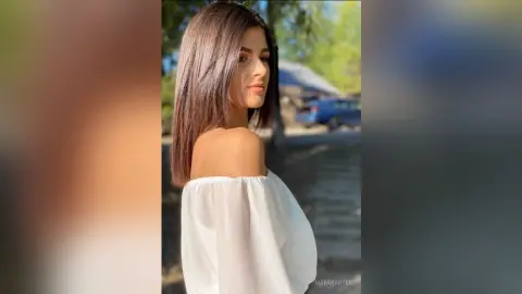 Young woman in a white off-the-shoulder blouse posing outdoors in soft natural sunlight.