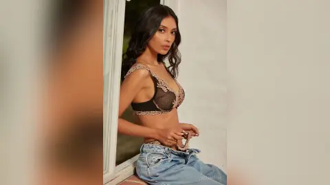 LucyMartin poses in black lace lingerie and light blue denim jeans against a white wall.