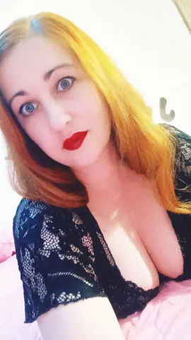 Jill_Stevens poses in a black lace top, showing off her cleavage and long blonde hair with red lipstick.