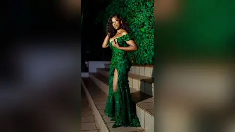 Elegant woman in a glamorous emerald green sequin gown posing on outdoor stairs against a lush garden backdrop.