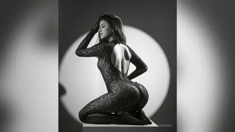 Elegant woman in a black lace bodysuit posing in a moody black and white studio setting.