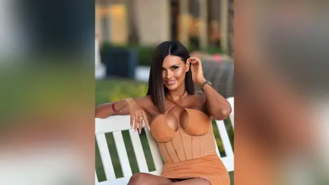 Glamorous woman in a tan corset dress sitting on a white bench in a soft outdoor setting.