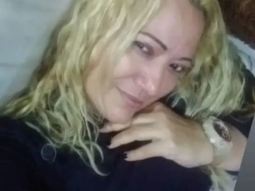 Smiling blonde woman in a black top relaxing in a cozy indoor setting with a peaceful mood.