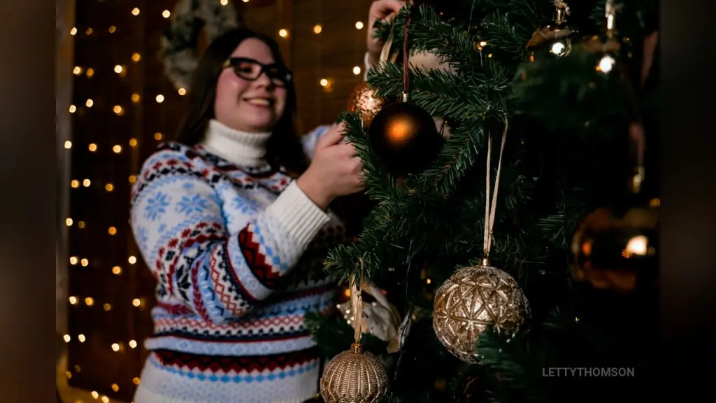 Smiling young woman with long brown hair and black glasses wearing a red lace top in a bright indoor setting.
