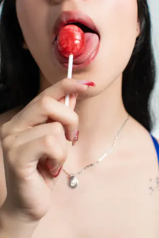 Susanmaeda licks a large red lollipop with her tongue out, looking into the camera.