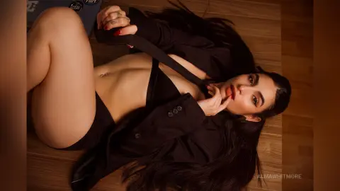 Glamorous woman in a black blazer and lingerie lying on a wooden floor with a moody, cinematic aesthetic.