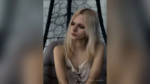 JaunitaHereth is a blonde woman wearing a white tank top while sitting in a hanging chair.