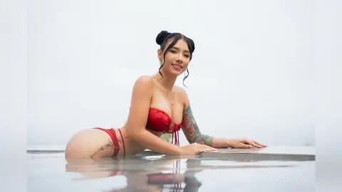 Smiling woman in a red bikini relaxing in a luxury infinity pool against a bright, misty background.