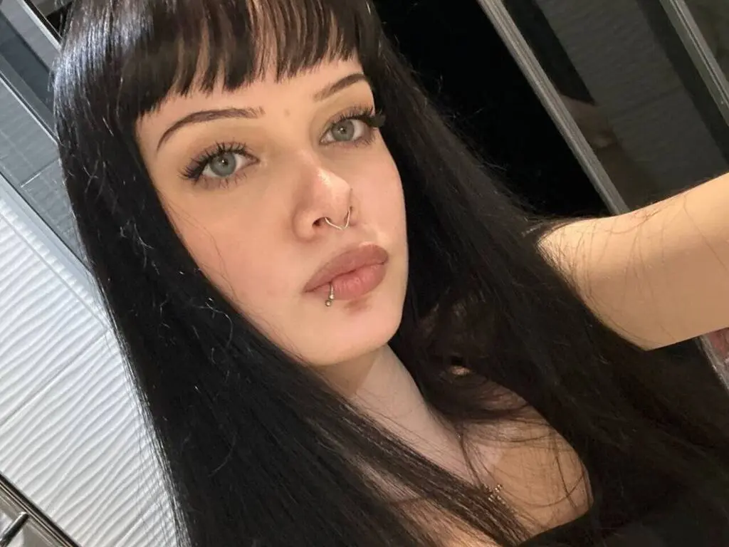 Young woman with long dark hair and nose ring posing for a selfie in a modern indoor setting.