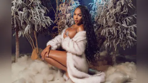 Glamorous woman in a white faux fur coat posing amidst snowy winter trees in a dreamy holiday setting.