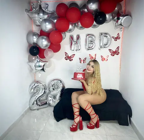 Blonde woman in a red dress celebrating her 28th birthday with red and silver balloons and a cake.