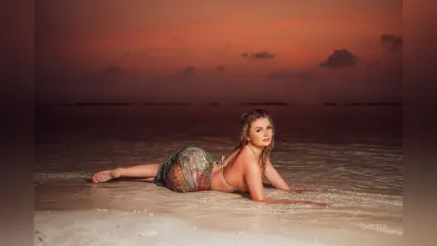 Beautiful woman in a patterned bikini relaxing on a sandy beach during a warm sunset.
