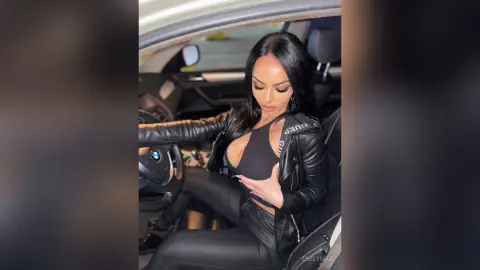 Glamorous woman in a black leather jacket and crop top sitting in a luxury car interior.