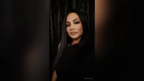 Elegant woman with long dark hair wearing a black outfit against a dark moody background.