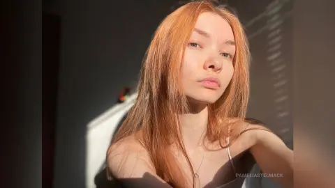 Redheaded woman in a grey tank top posing in warm, cinematic sunlight for a moody portrait.
