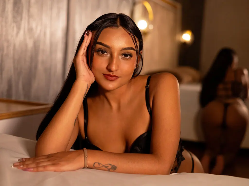 Young woman with long brown hair in a black crop top posing in a bright room with green ivy decor.