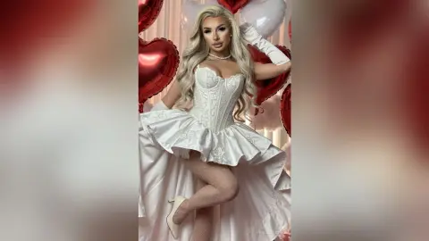 Glamorous blonde woman in a white corset gown posing amidst red heart balloons for a romantic celebration.