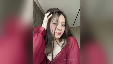 Young woman with long brown hair wearing a romantic burgundy long-sleeve blouse in a modern indoor setting.