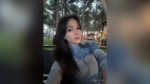 Smiling young woman in a blue denim top relaxing in a peaceful outdoor forest setting.