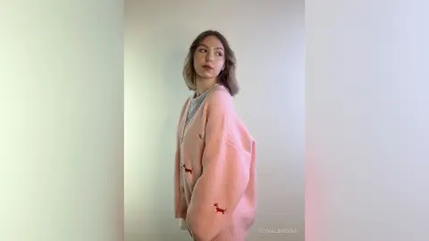 Young woman in a cozy pink oversized cardigan with red dachshund embroidery standing against a white wall.
