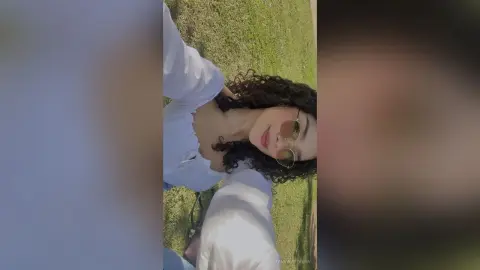 Smiling young woman in a white shirt and sunglasses relaxing outdoors on a sunny day.